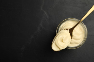 Jar of delicious mayonnaise and spoon on black table, top view. Space for text