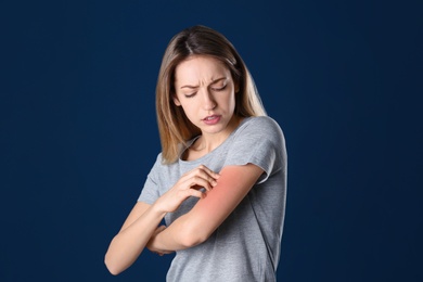 Portrait of woman scratching arm on color background. Allergy symptom