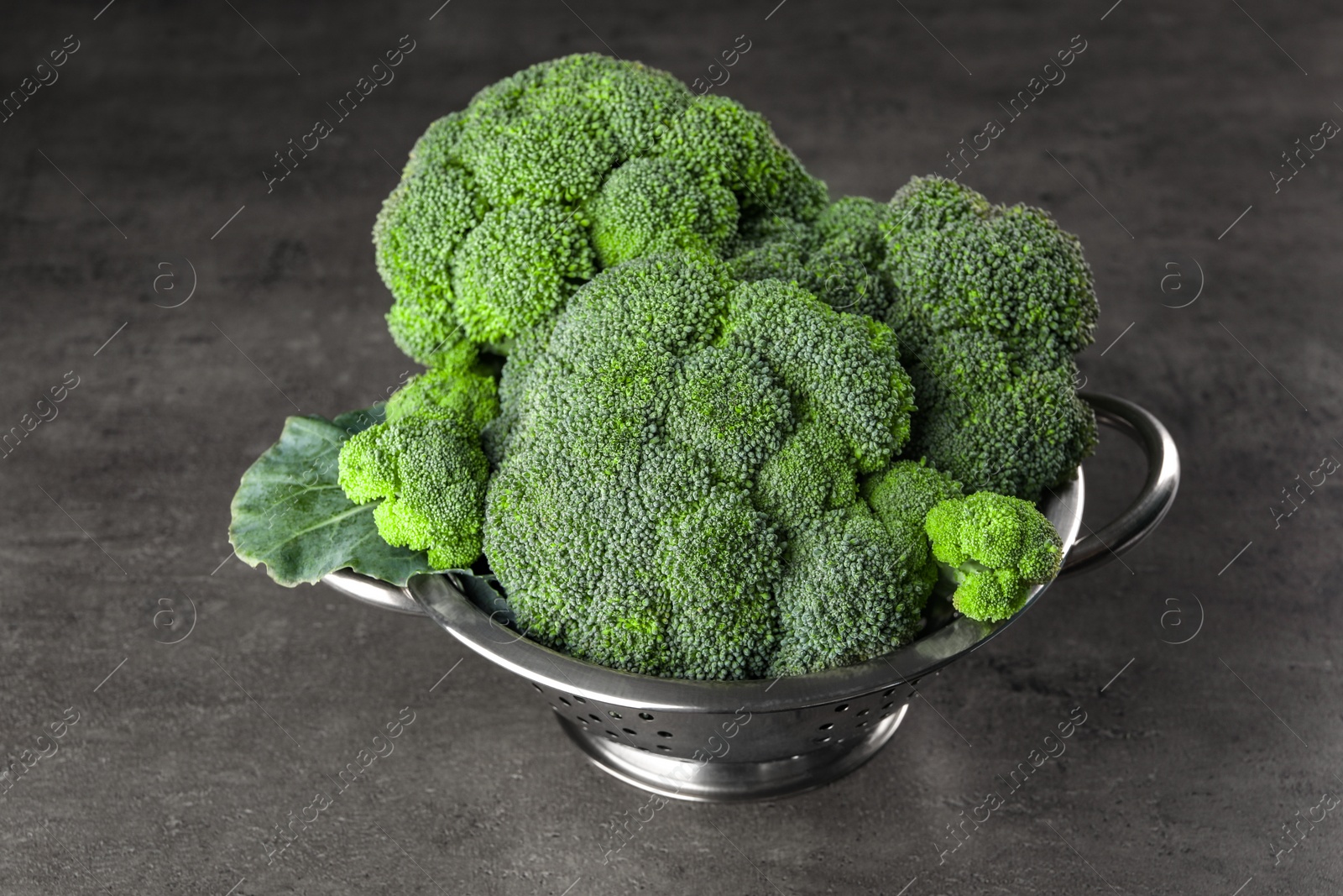 Photo of Colander with fresh raw broccoli on grey table