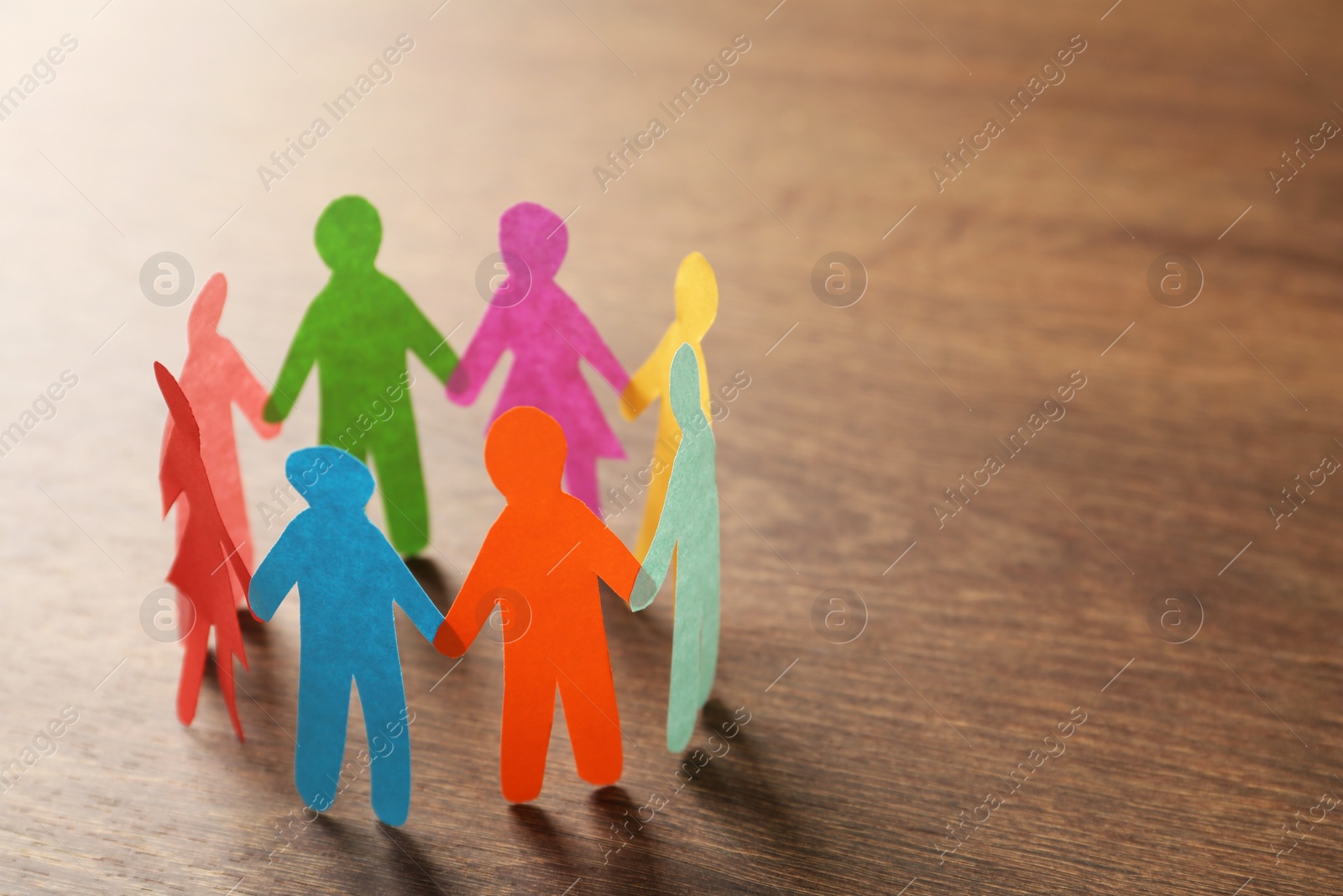 Photo of Many different paper human figures standing in circle on wooden table, space for text. Diversity and inclusion concept