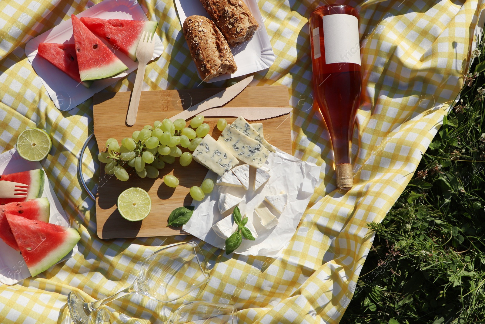 Photo of Picnic blanket with delicious food and wine on green grass outdoors, top view