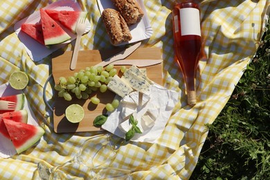 Picnic blanket with delicious food and wine on green grass outdoors, top view