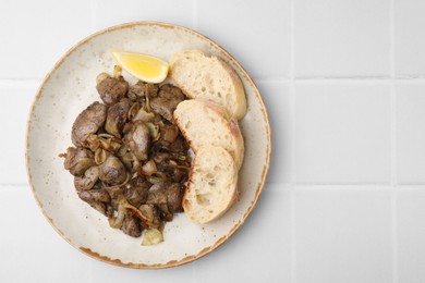 Tasty fried chicken liver served with lemon and bread on white tiled table, top view. Space for text