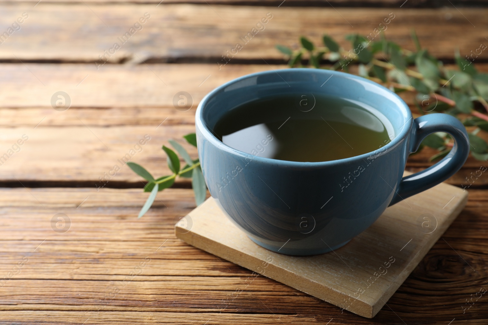 Photo of Cup of green tea and eucalyptus leaves on wooden table. Space for text