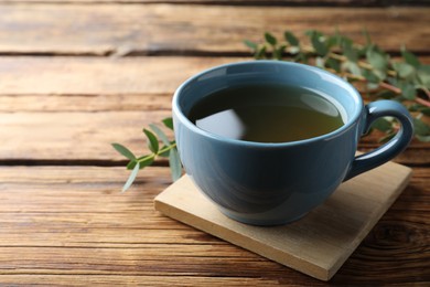 Cup of green tea and eucalyptus leaves on wooden table. Space for text