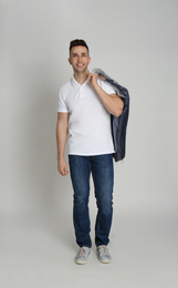 Man holding hanger with jacket in plastic bag on light grey background. Dry-cleaning service