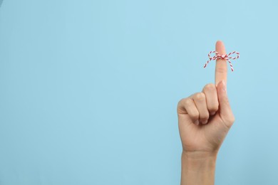 Woman showing index finger with tied bow as reminder on light blue background, closeup. Space for text