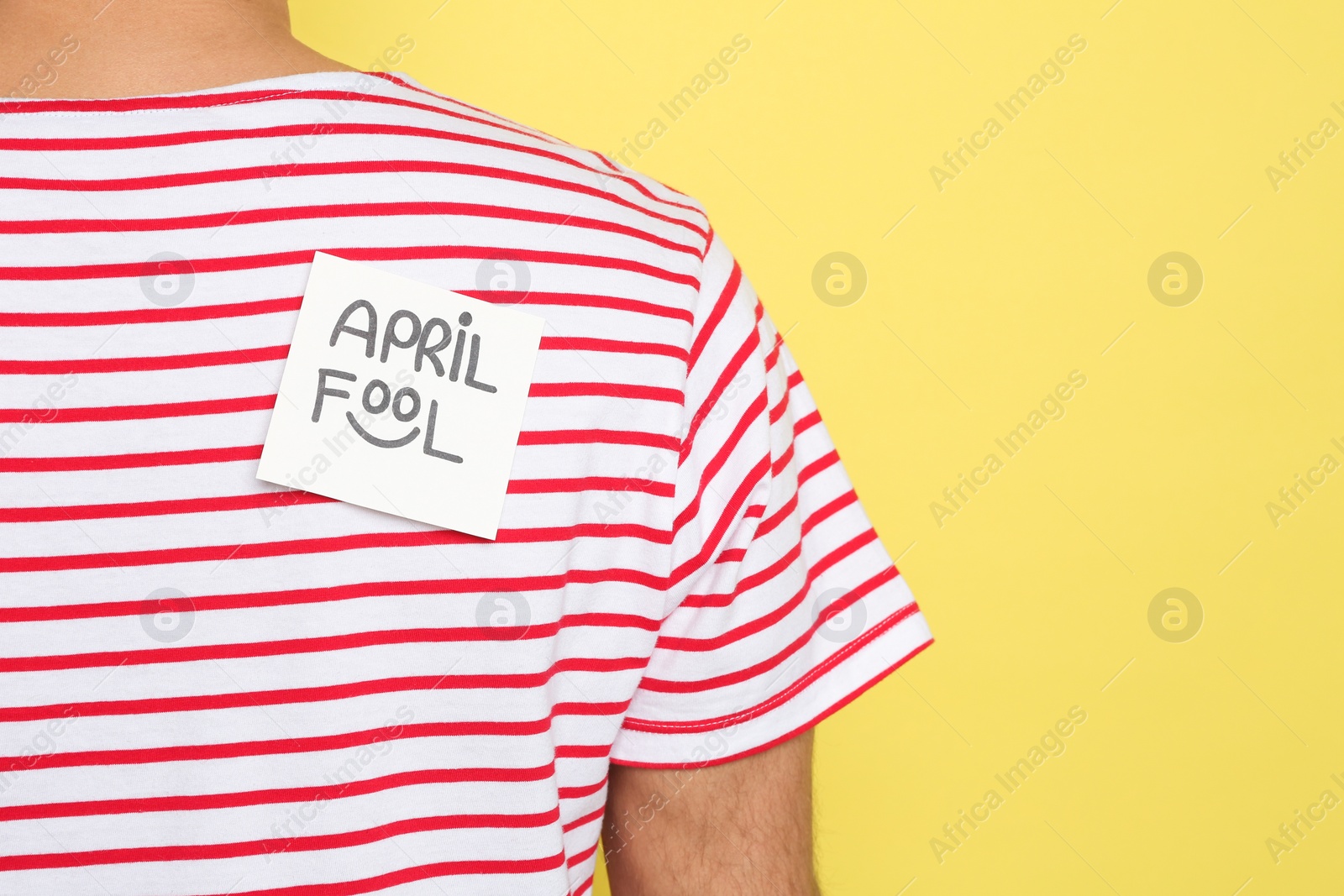 Photo of Man with APRIL FOOL sticker on back against yellow background, closeup