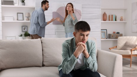 Photo of Couple arguing at home, focus on their unhappy teenage boy. Problems in family