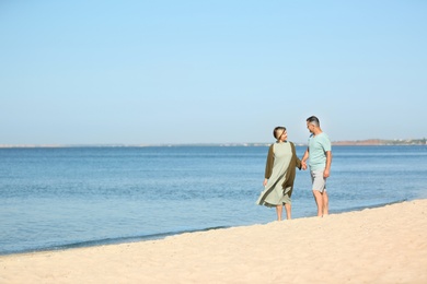 Happy mature couple walking at beach on sunny day