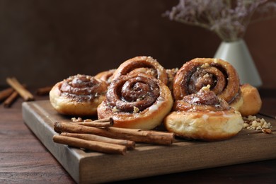 Photo of Tasty cinnamon rolls, sticks and nuts on wooden table