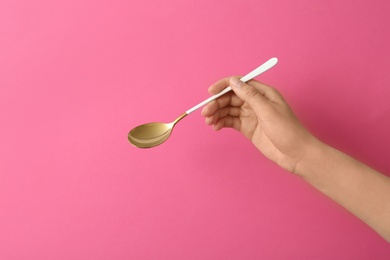 Photo of Woman holding empty table spoon on color background, closeup