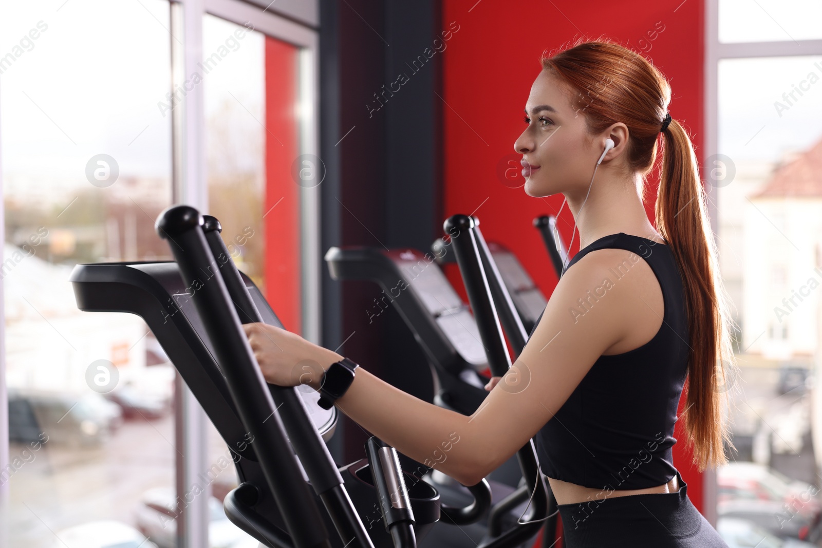 Photo of Athletic young woman with earphones doing exercise with air walker in gym