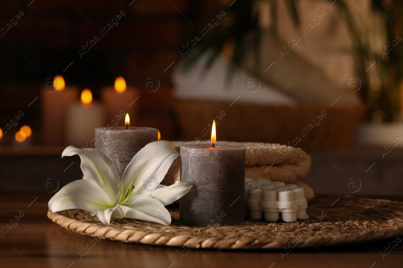 Photo of Spa composition with burning candles, lily flower and towels on wooden table in wellness center