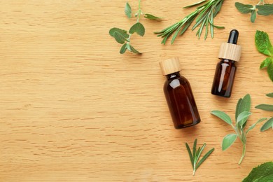 Photo of Bottles of essential oils and fresh herbs on wooden table, flat lay. Space for text