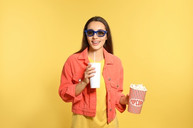 Woman with 3D glasses, popcorn and beverage during cinema show on color background