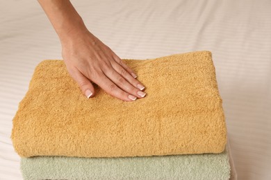 Photo of Woman touching soft towels on bed, closeup view