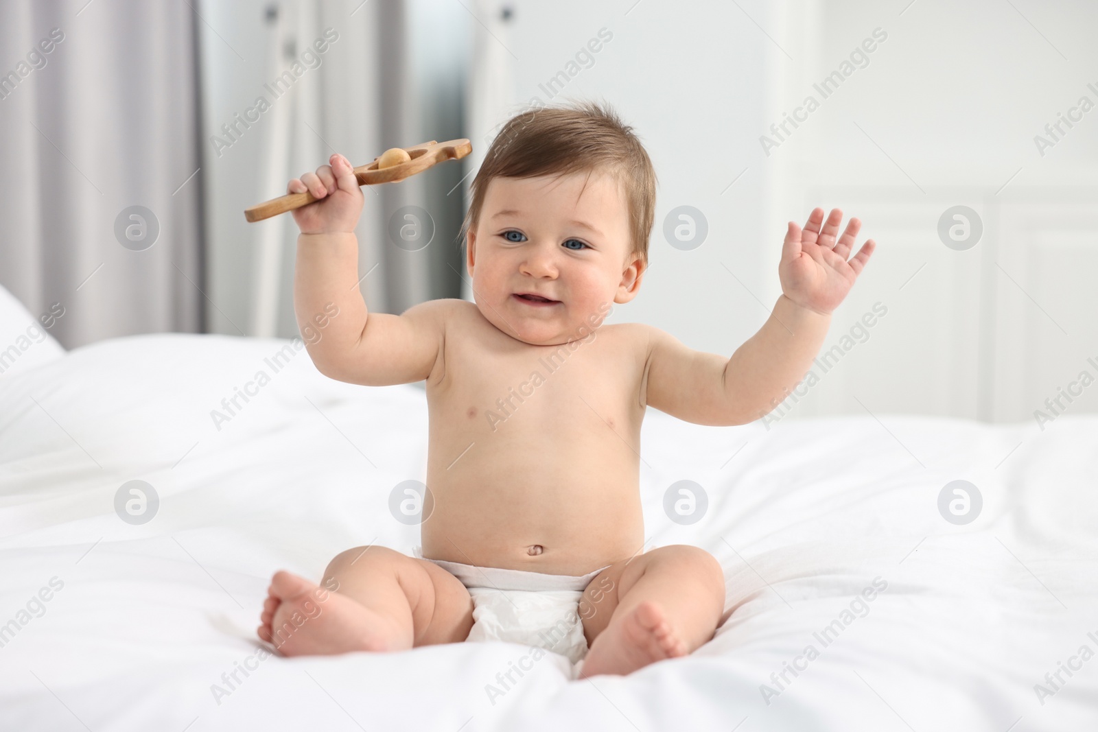 Photo of Cute baby boy with wooden rattle on bed at home