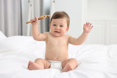 Photo of Cute baby boy with wooden rattle on bed at home