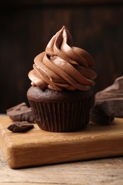 Photo of Delicious cupcake with cream and chocolate pieces on wooden table, closeup