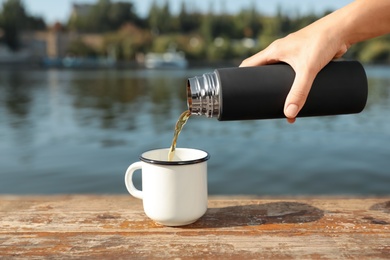 Woman pouring hot drink from thermos into cup outdoors, closeup