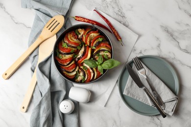 Delicious ratatouille, chili peppers and cutlery on white marble table, flat lay