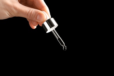 Woman holding pipette with oil on black background. Space for text