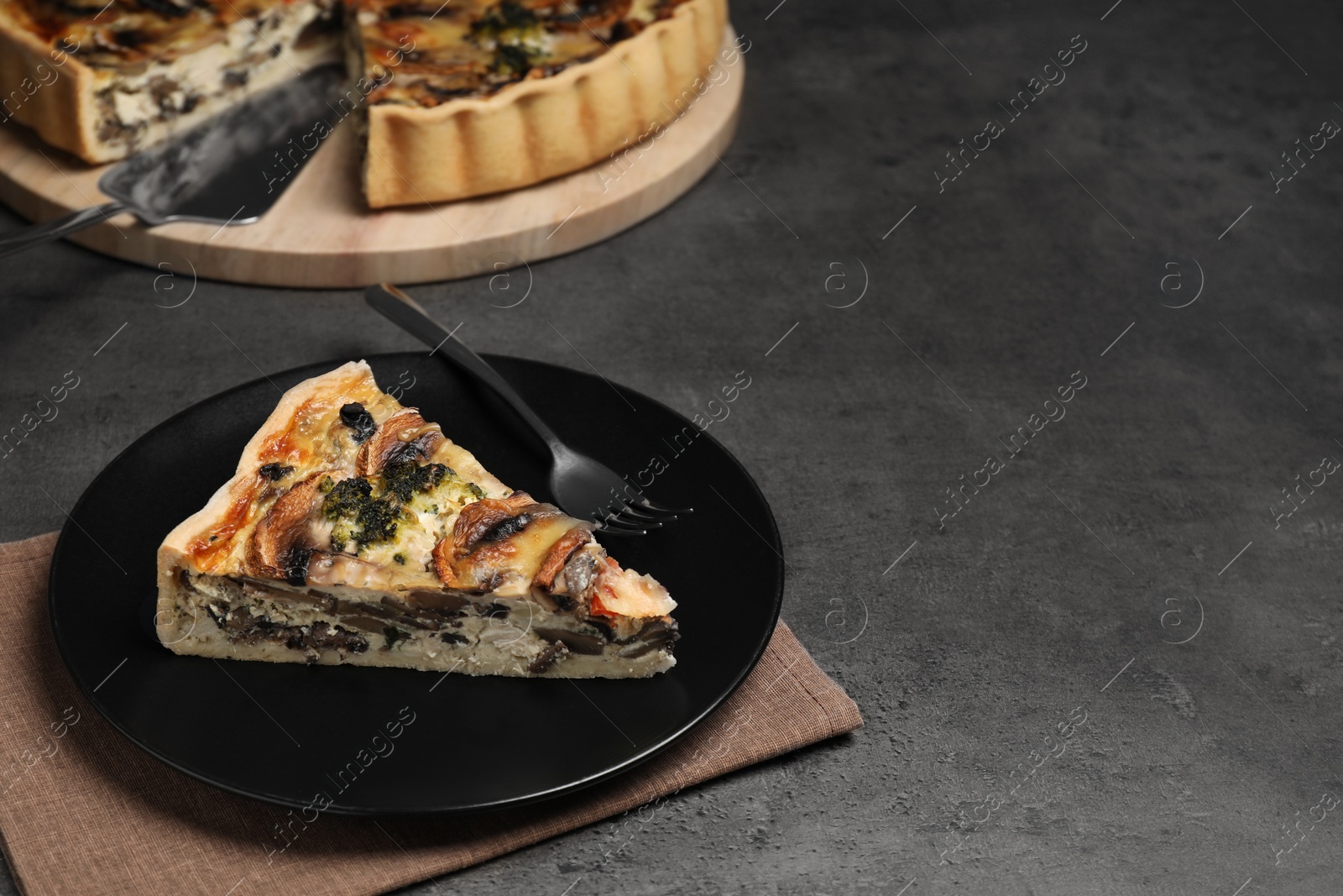Photo of Piece of delicious quiche with mushrooms on dark grey table. Space for text