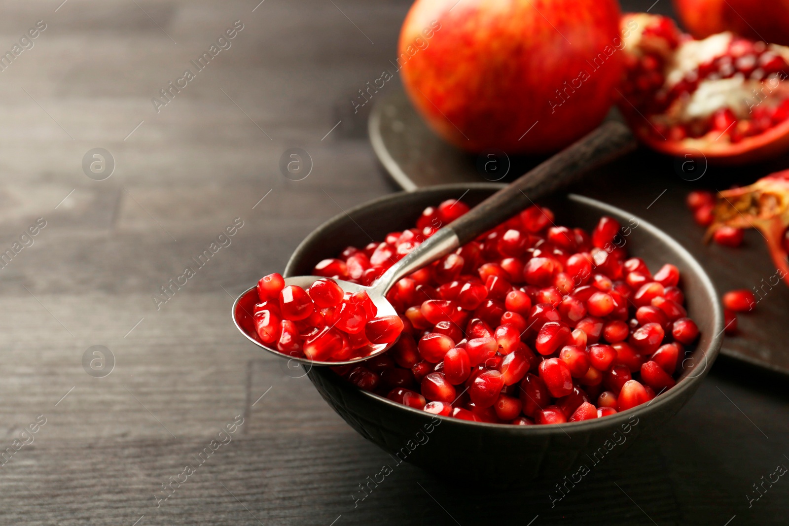 Photo of Tasty ripe pomegranates and grains on dark wooden table, closeup. Space for text