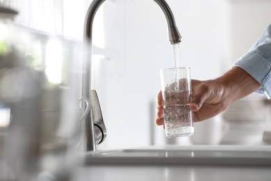 Photo of Man pouring water into glass in kitchen, closeup