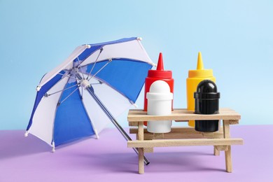 Photo of Different sauces and spices in wooden holder near toy umbrella on color background. Kitchen rack