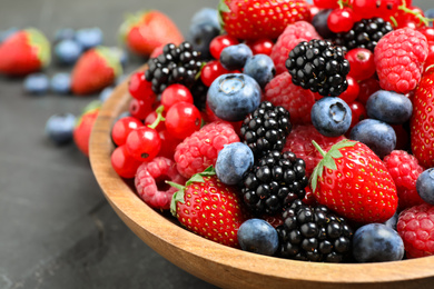 Mix of different fresh berries in bowl on grey table, closeup