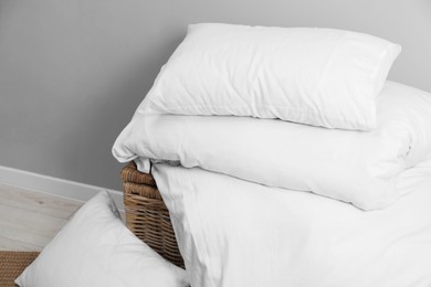 Soft pillows, duvet and wicker trunk near grey wall indoors