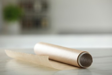 Photo of Roll of baking paper on white marble table against blurred background indoors