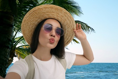 Image of Beautiful woman in straw hat taking selfie at resort