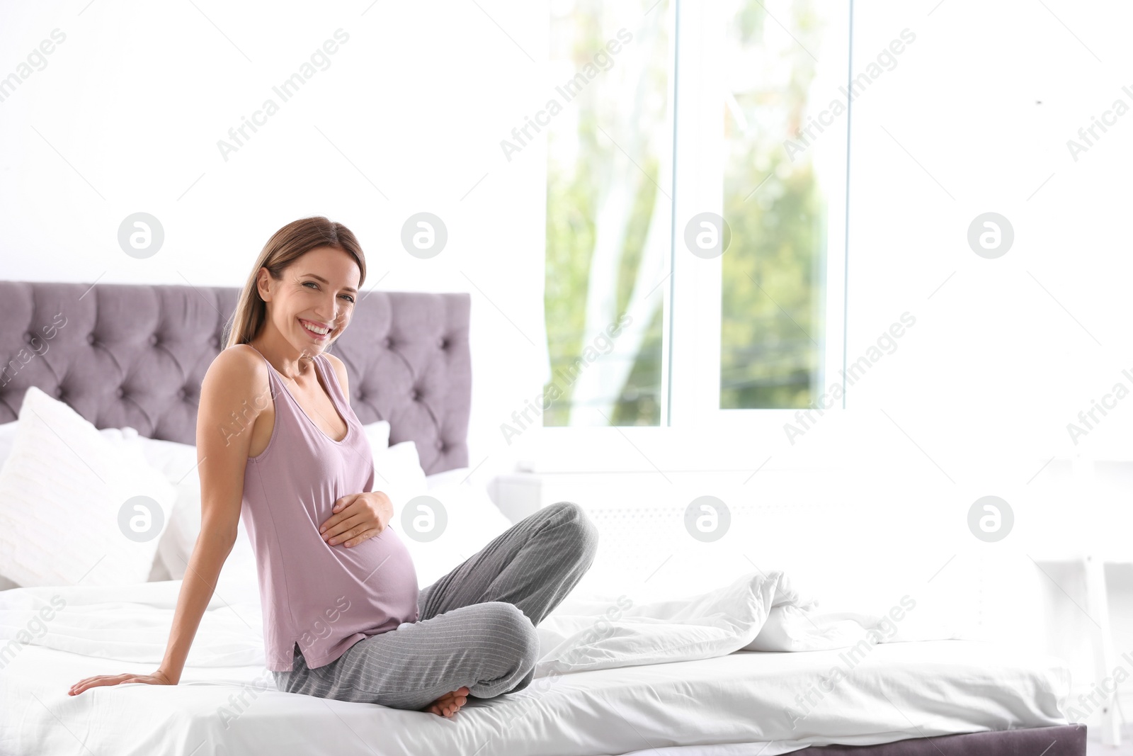 Photo of Happy pregnant woman sitting in bed at home