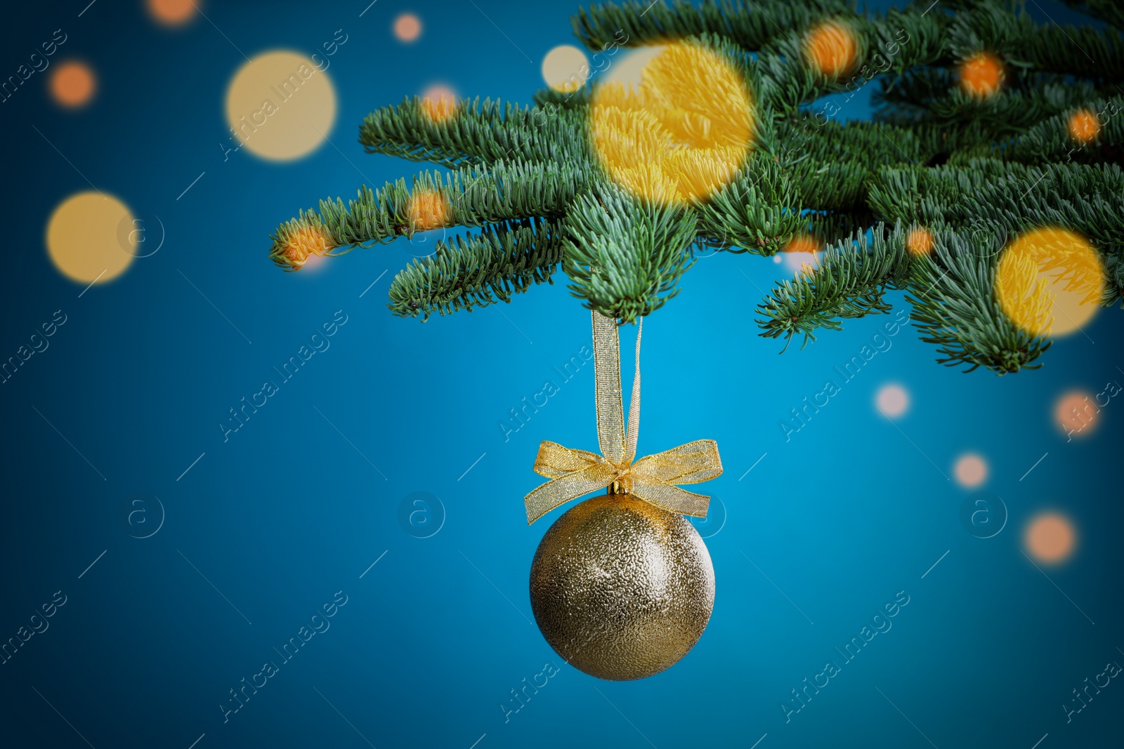 Photo of Beautiful Christmas ball hanging on fir tree branch against light blue background, bokeh effect