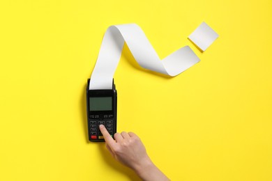 Photo of Woman using payment terminal with thermal paper for receipt on yellow background, top view