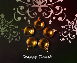 Image of Inscription Happy Diwali and clay lamps on dark background, flat lay 