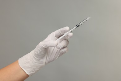 Doctor holding medical syringe on grey background, closeup