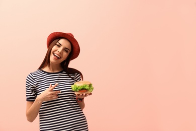 Young woman with tasty burger on color background. Space for text
