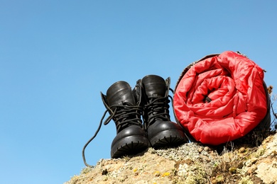 Photo of Boots and sleeping bag on rock outdoors, space for text. Camping equipment