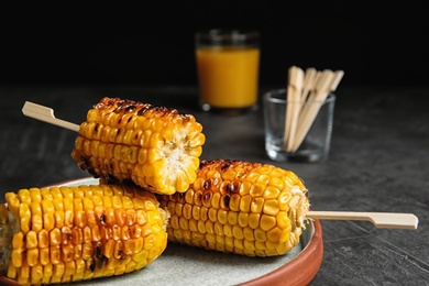 Photo of Plate with delicious grilled corn cobs on gray table against black background