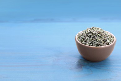 Photo of Ceramic bowl with dried thyme on light blue wooden table. Space for text
