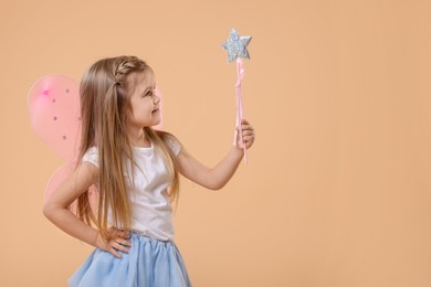 Photo of Cute little girl in fairy costume with pink wings and magic wand on beige background, space for text