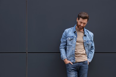 Handsome bearded man leaning to grey wall outdoors. Space for text