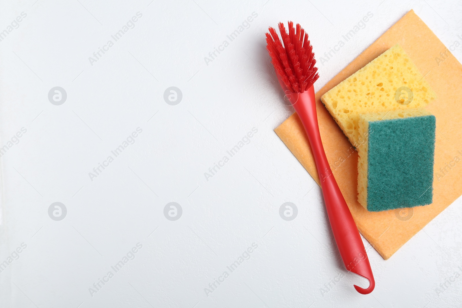 Photo of Cleaning brush, sponges and rag on white background, flat lay with space for text. Dish washing supplies