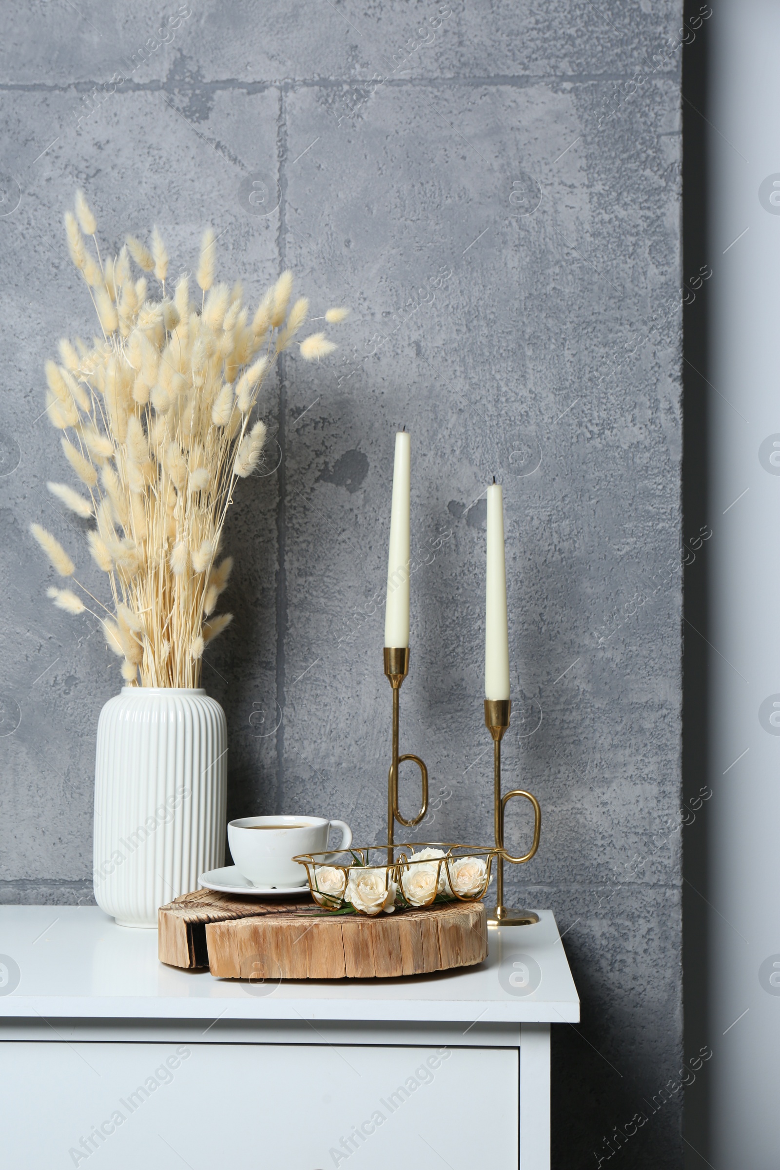 Photo of Cup of coffee, vase and other decor on white table near grey wall indoors. Interior design