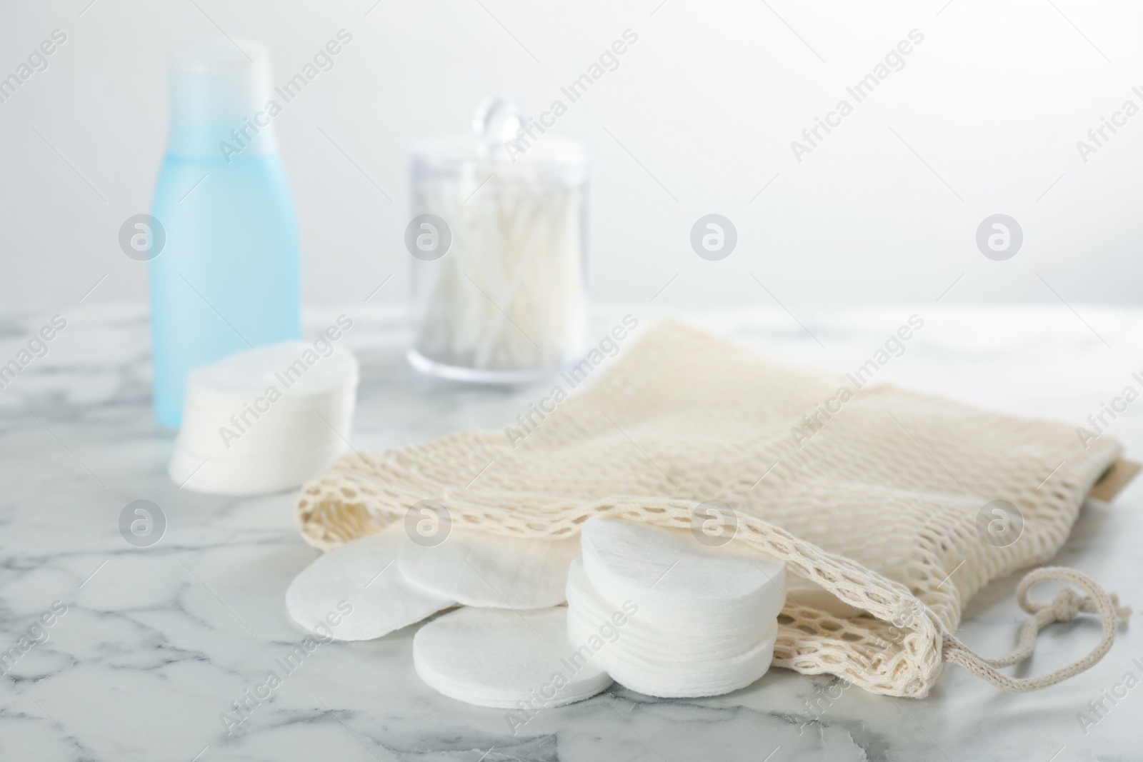 Photo of Cotton pads and makeup removal product on white marble table