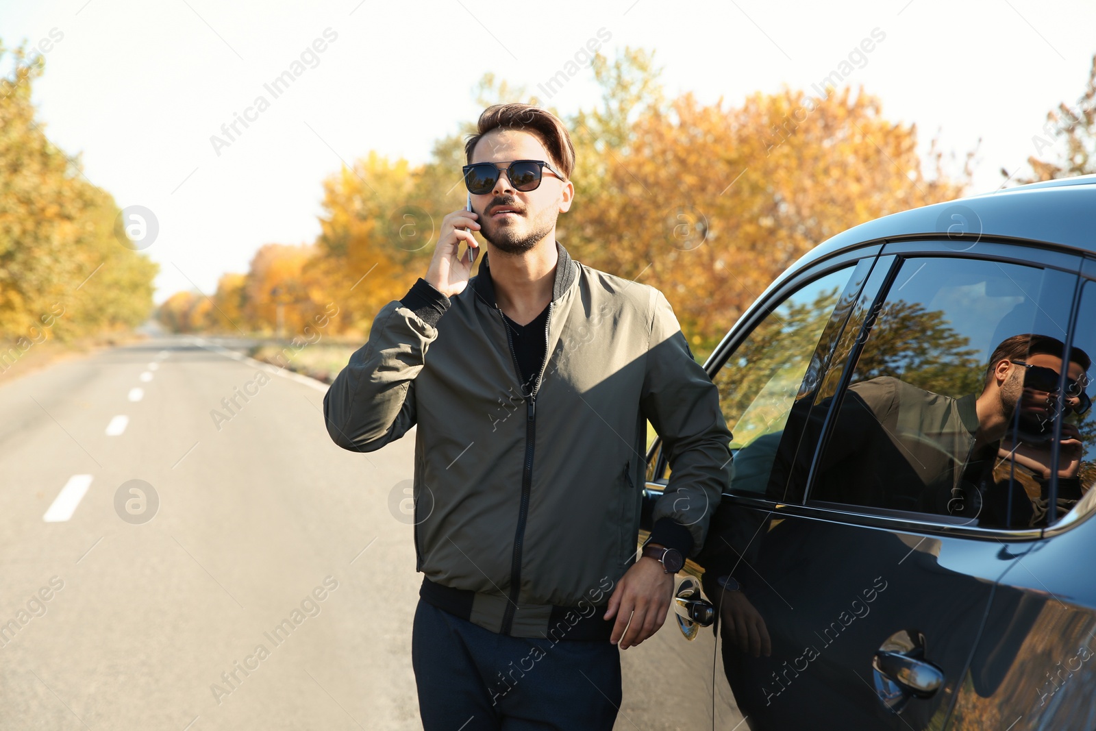 Photo of Young man talking on phone near modern car, outdoors